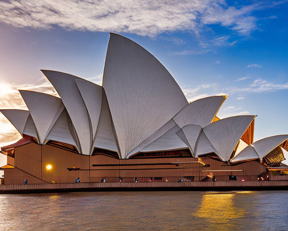 Iconic Sydney Opera House at sunset with sail-like design against blue sky and tranquil harbor reflection