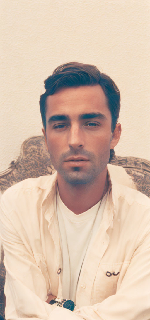 Dark-haired man in buttoned shirt on cream background