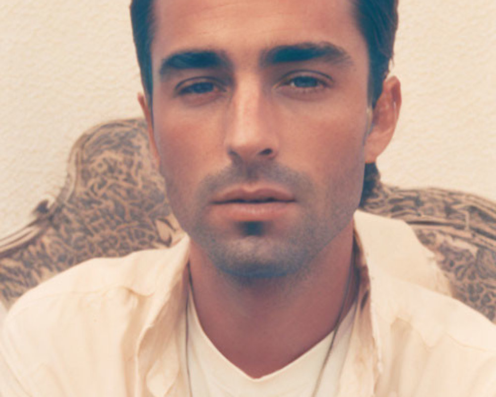 Dark-haired man in buttoned shirt on cream background