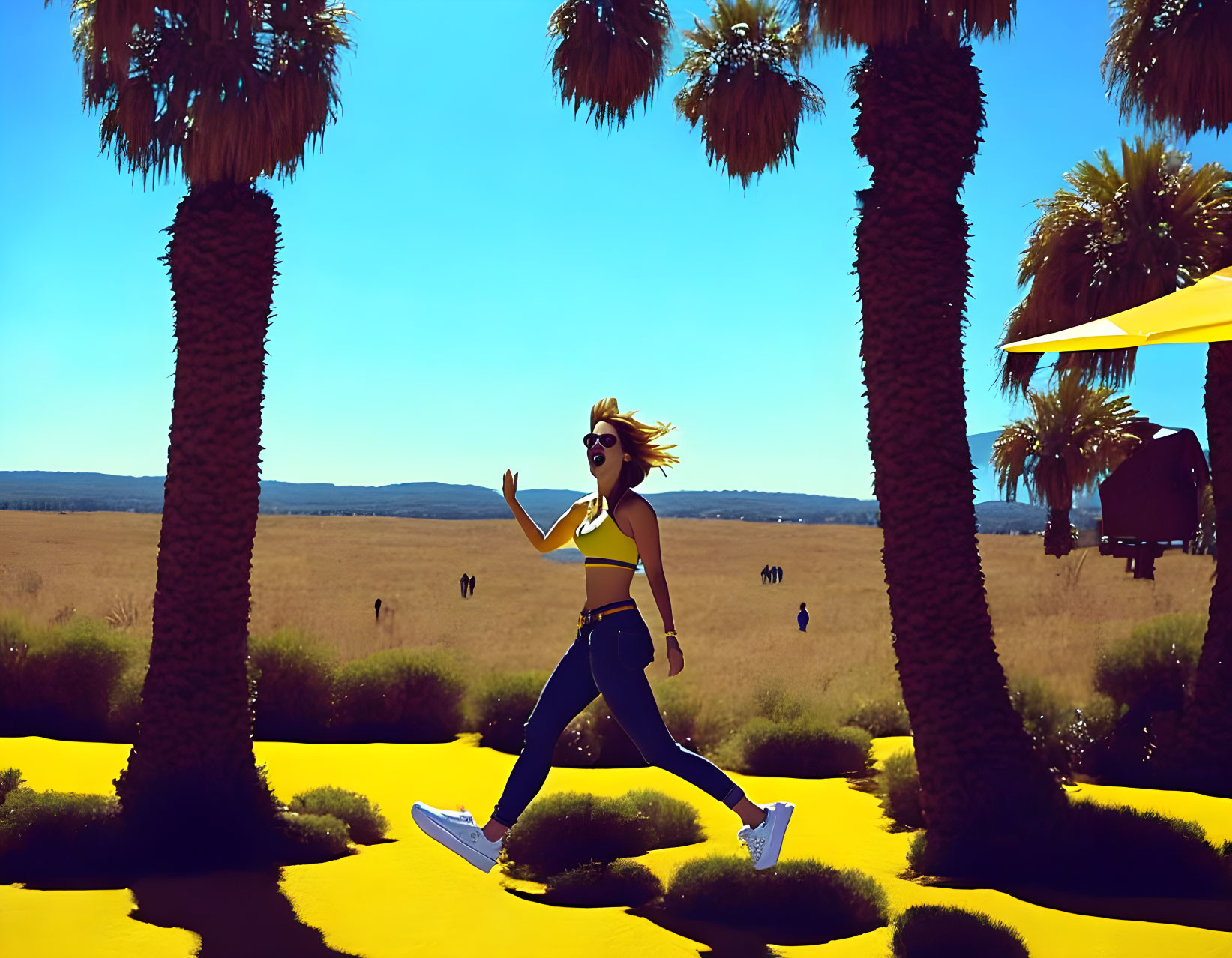 Joyful woman jumps between palm trees on bright yellow pathway under clear blue sky