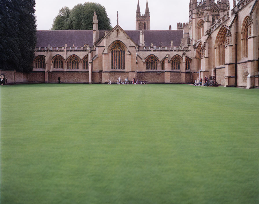 Gothic-style building with arched windows and lush green lawn, people and bicycles in the scene