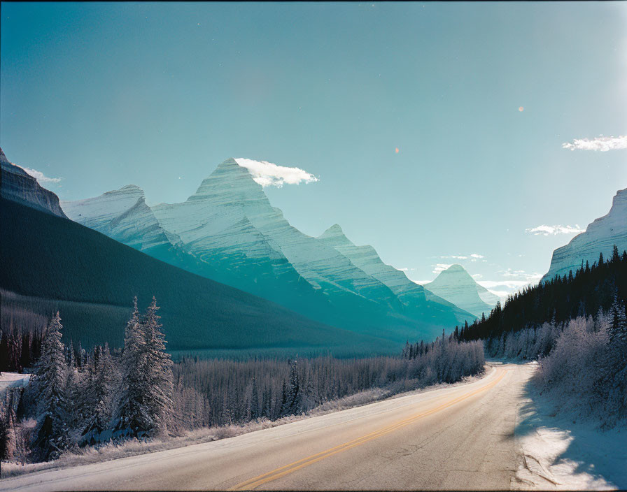 Snowy forest winter road with mountains under blue sky