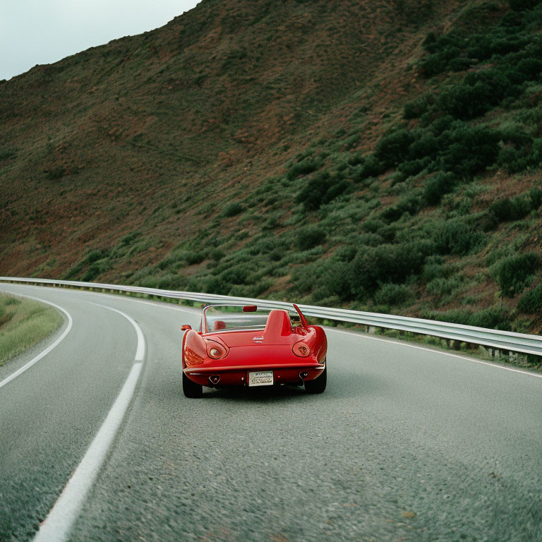 Classic Red Convertible Car on Curved Road with Green Hills Background