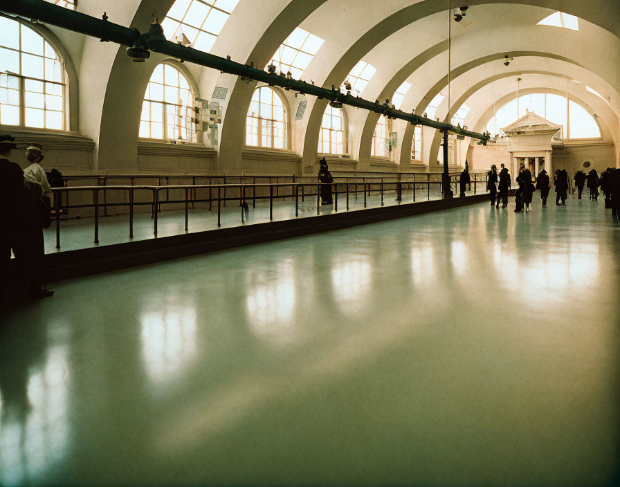 Large indoor gallery with high ceiling, reflective floor, and arched windows showcasing exhibits.