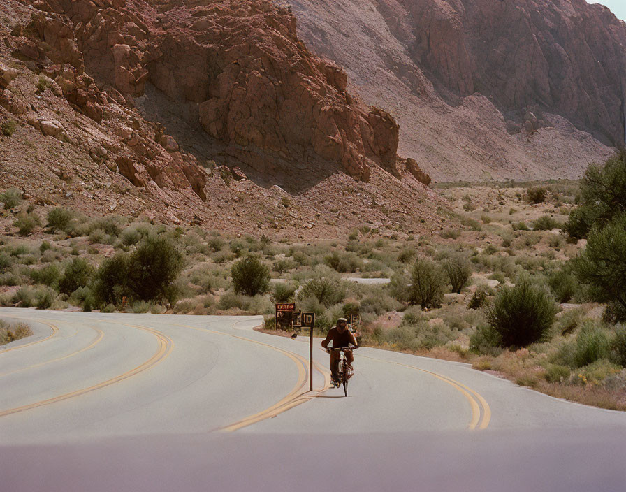 Cyclist on winding desert road with rocky cliffs