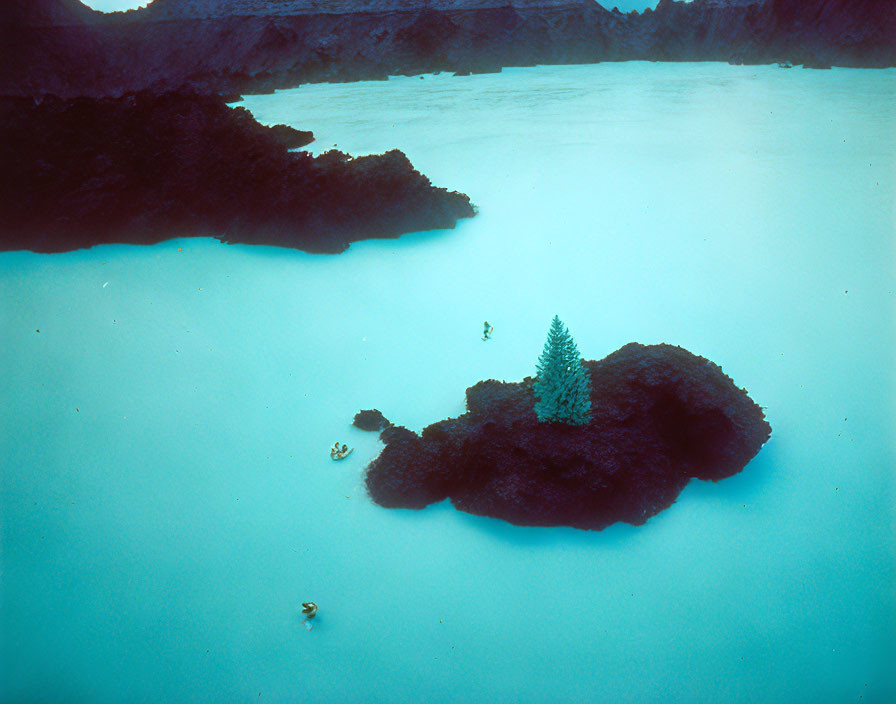 Tranquil blue lagoon with rocky island, swimmers, and boat