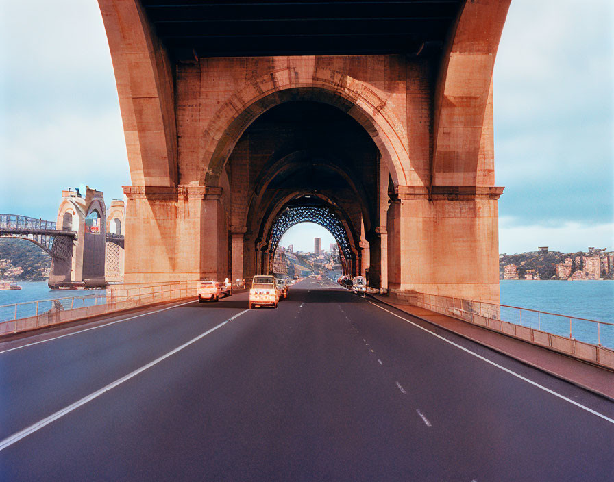 Vehicles under arch bridge with city skyline view