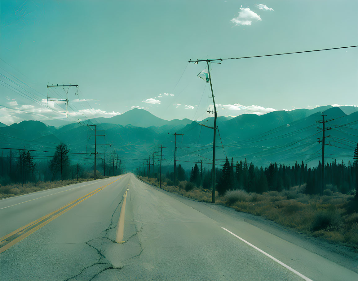 Deserted road with distant mountains, hazy sky, power lines, and arid vegetation.