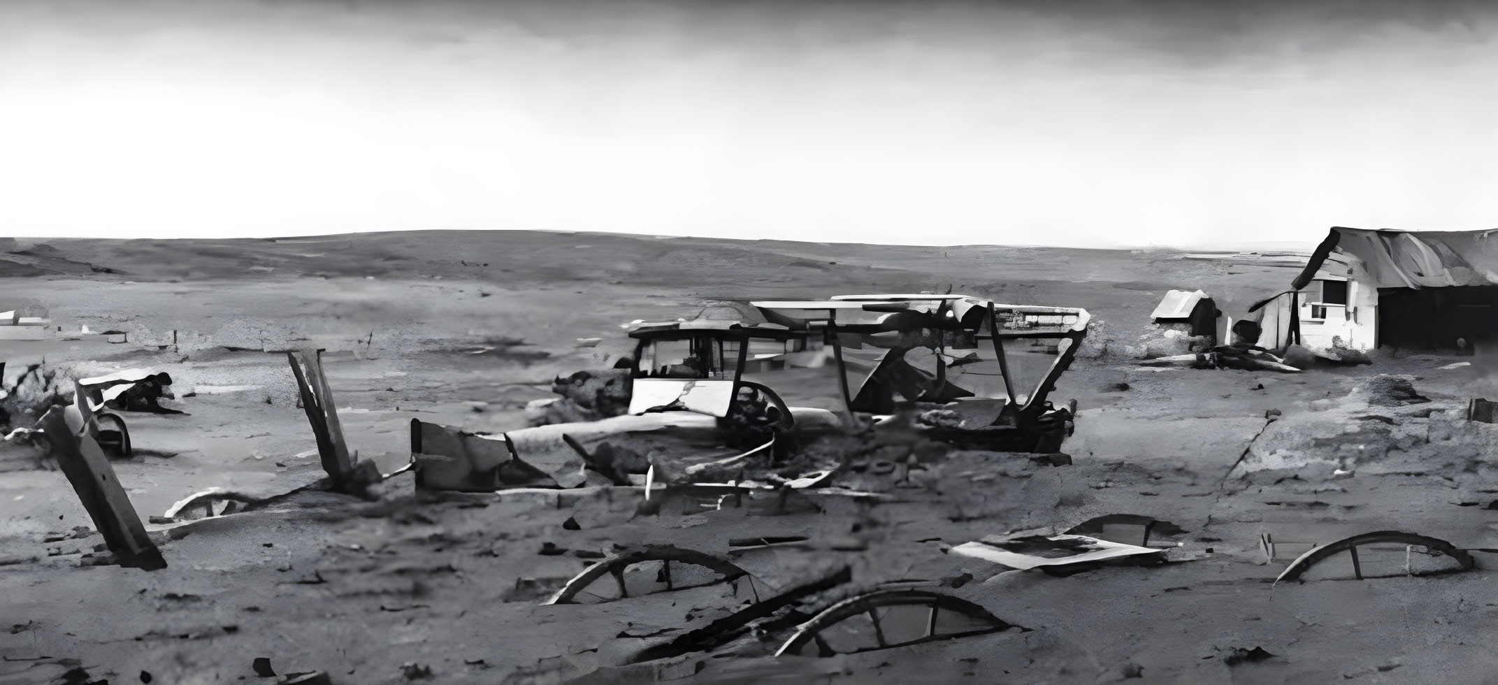 Desolate landscape with abandoned car and dilapidated building under cloudy sky