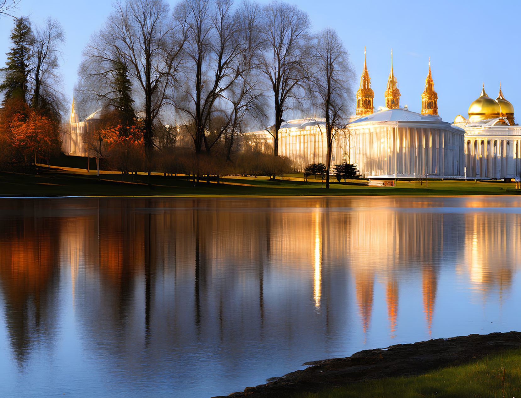 Golden-domed buildings and trees reflected in calm waters at tranquil dusk