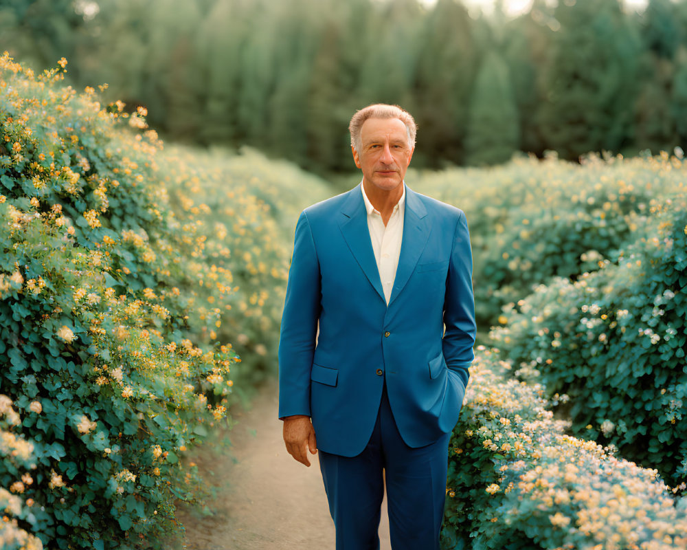 Man in Blue Suit Standing Confidently Among Green Shrubs