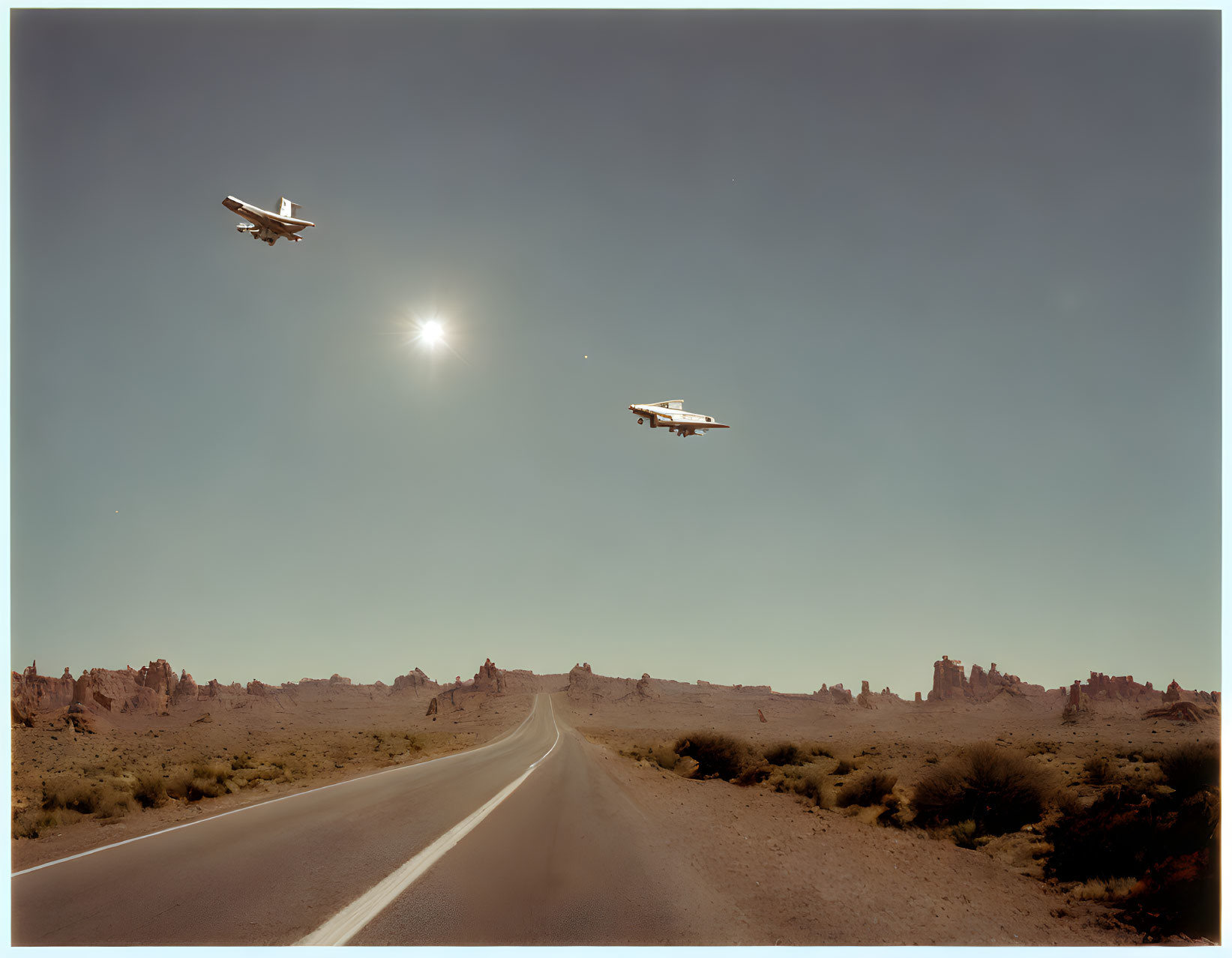 Low-flying planes over desert road with rock formations under clear sky.