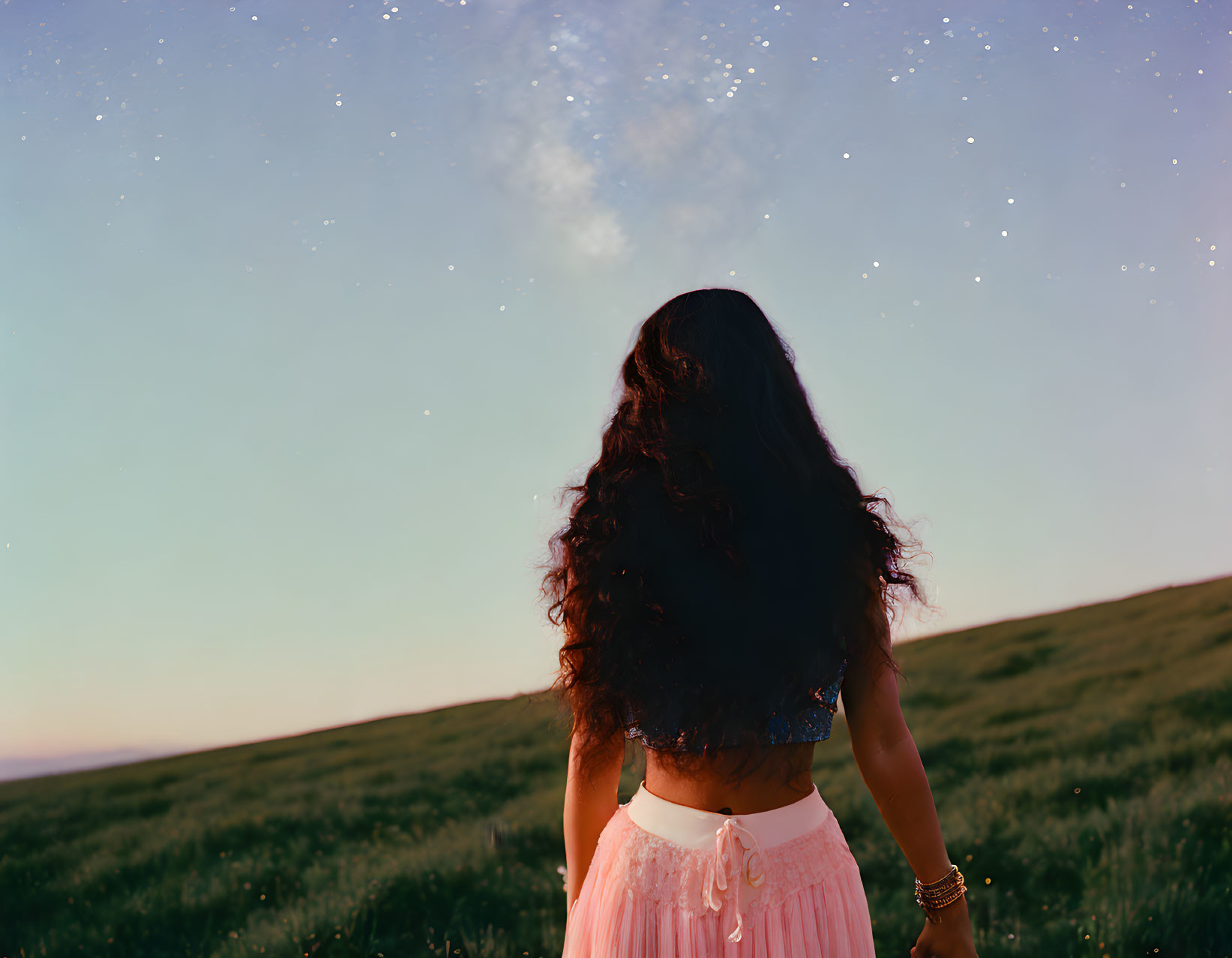 Dark-haired woman in grassy field at dusk under starry sky