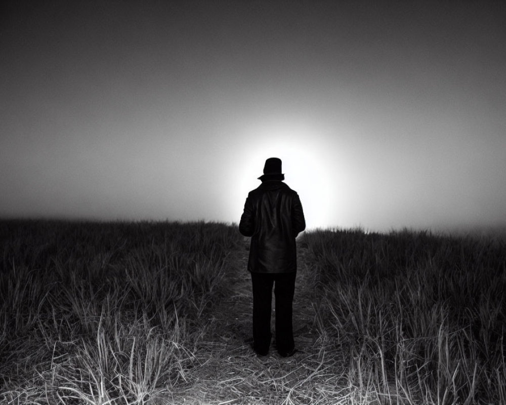 Mysterious figure in hat and coat standing in foggy field