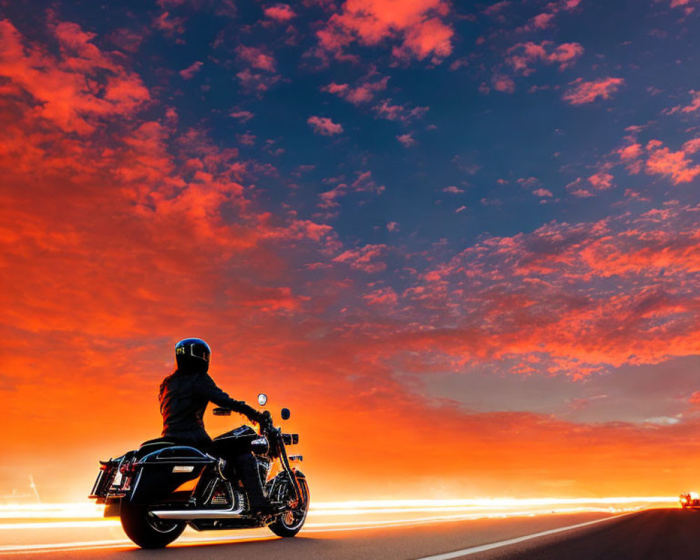 Motorcyclist riding on highway at sunset with vivid red and blue sky