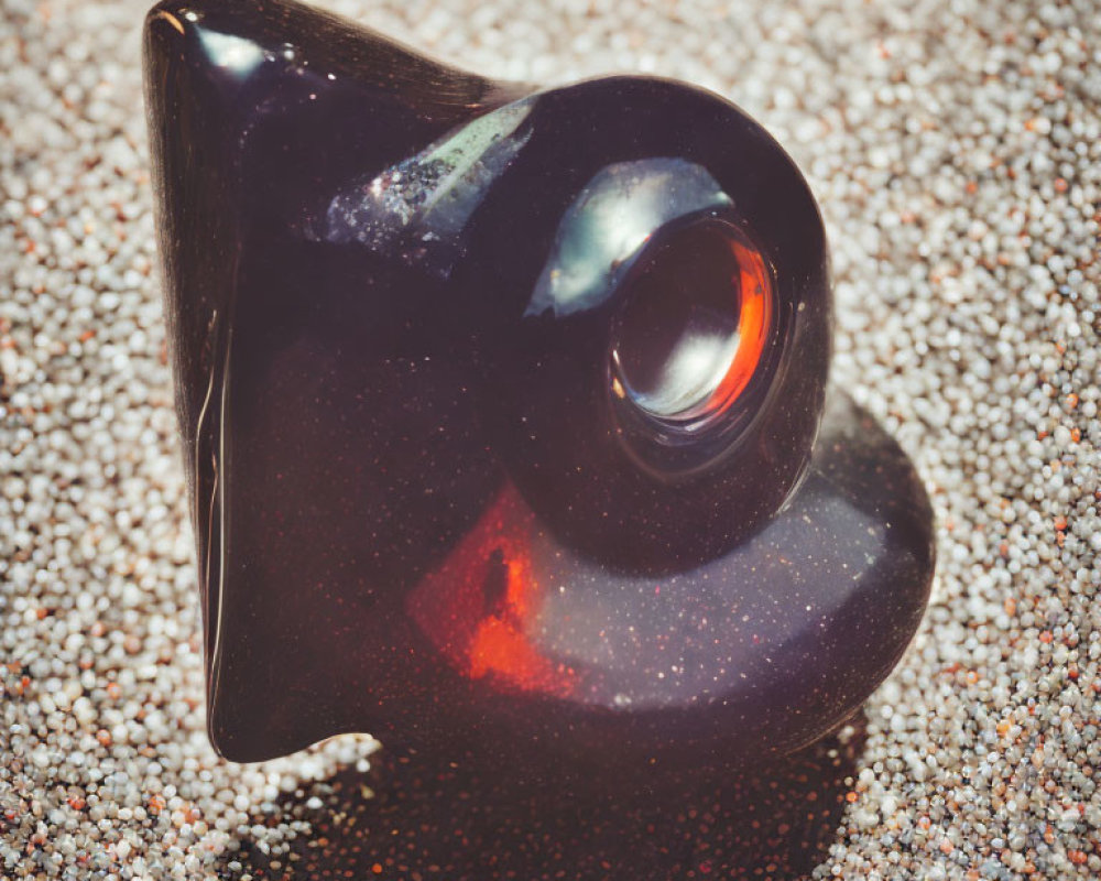 Dark Glass Sculpture with Swirling Form and Red Reflection on Sandy Surface