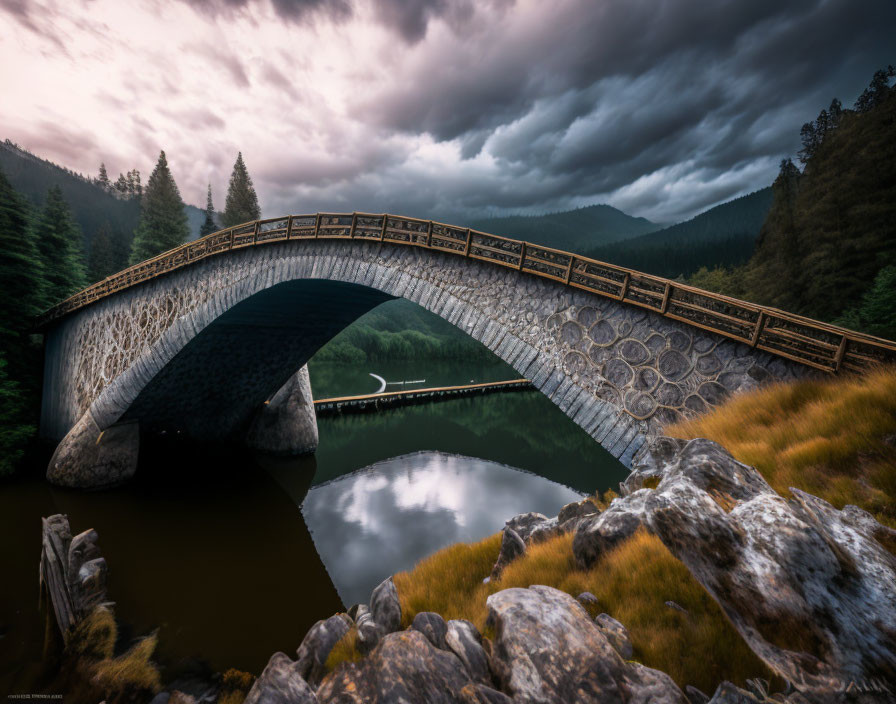 Stone arched bridge over river amidst forested mountains under dramatic sky