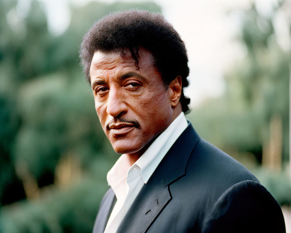 Man with Mustache and Curly Hair in Dark Jacket and Light Shirt gazes into Distance