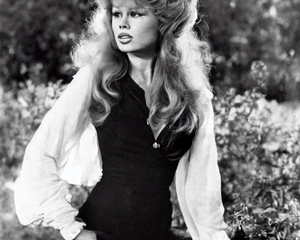 Monochrome portrait of woman with voluminous hair in low-cut top against natural background