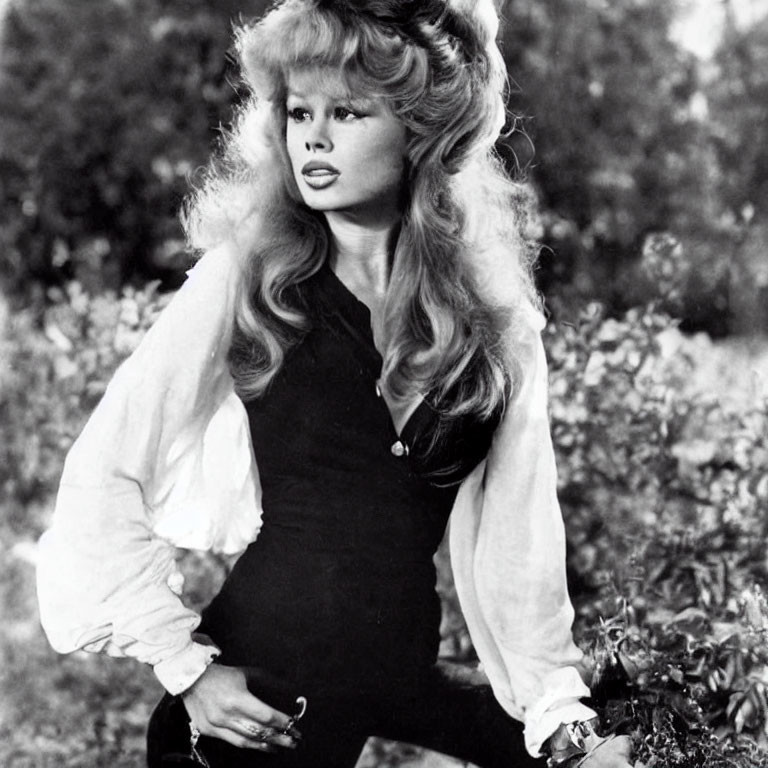 Monochrome portrait of woman with voluminous hair in low-cut top against natural background