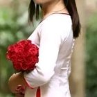 Woman in white dress with red ribbon holding red roses bouquet in blurred background