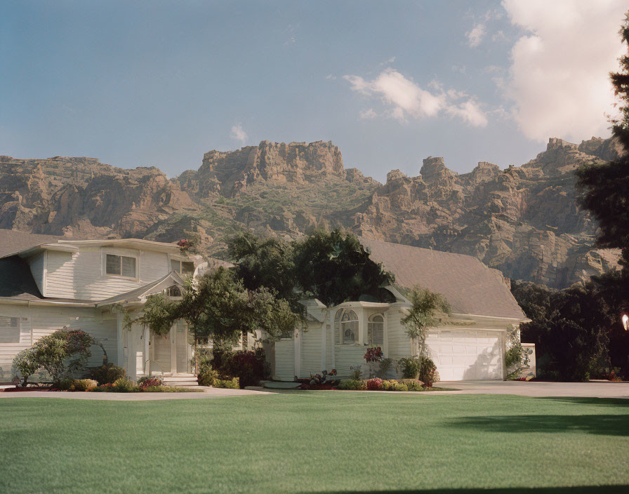 Suburban house with gabled roof, landscaped lawn, mountains, clear sky