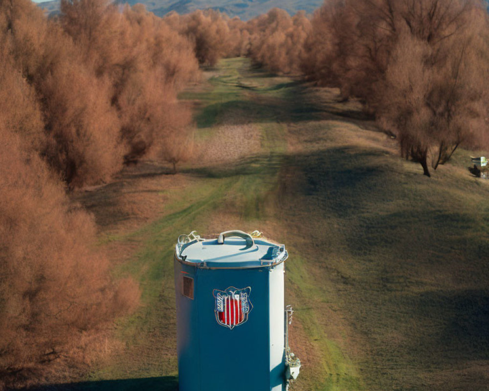 Blue cylindrical tank with logo in grassy landscape and hills under clear sky