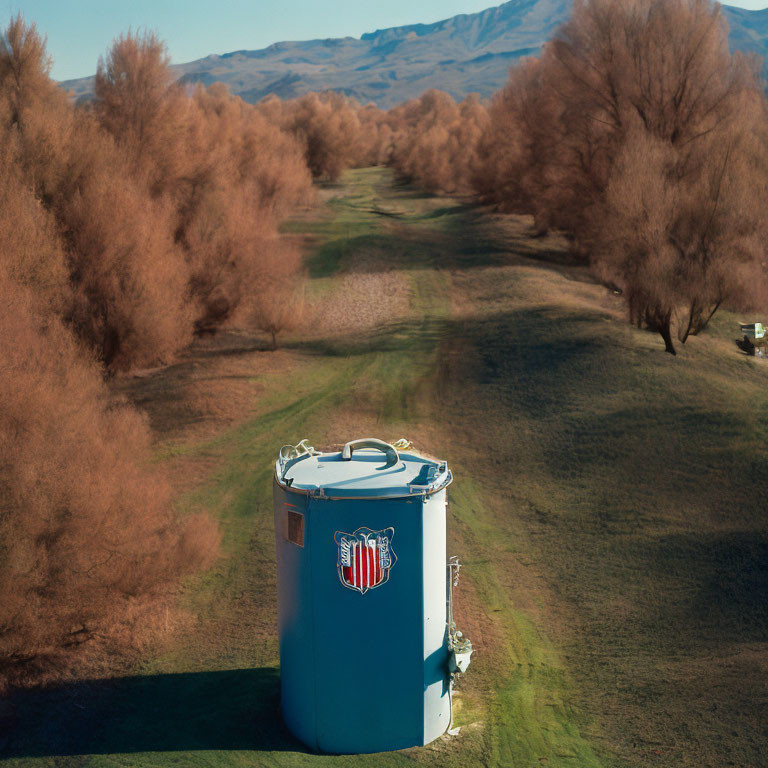 Blue cylindrical tank with logo in grassy landscape and hills under clear sky