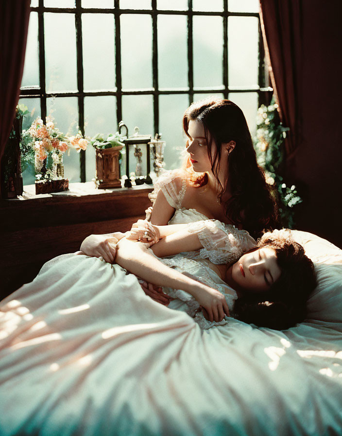 Two women in vintage dresses on bed with sunlight and flowers