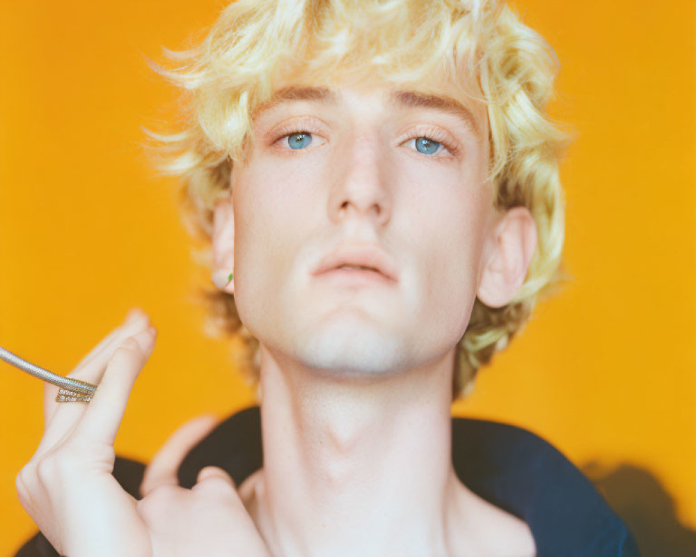 Curly Blond Hair and Blue Eyes Person Holding Pen on Orange Background