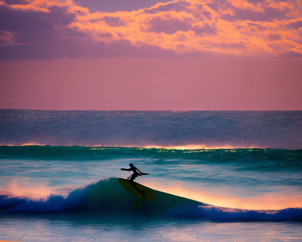 Surfer catching wave at vibrant purple and orange sunrise/sunset