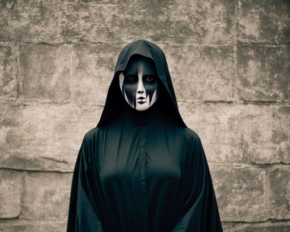 Black Cloaked Figure with White and Black Face Makeup Against Grey Wall