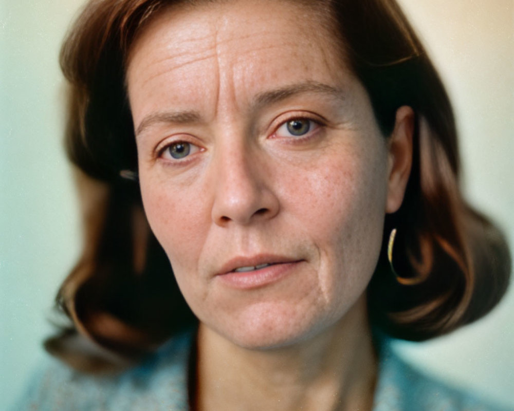 Brown-haired woman in blue top and earrings, close-up portrait with neutral expression