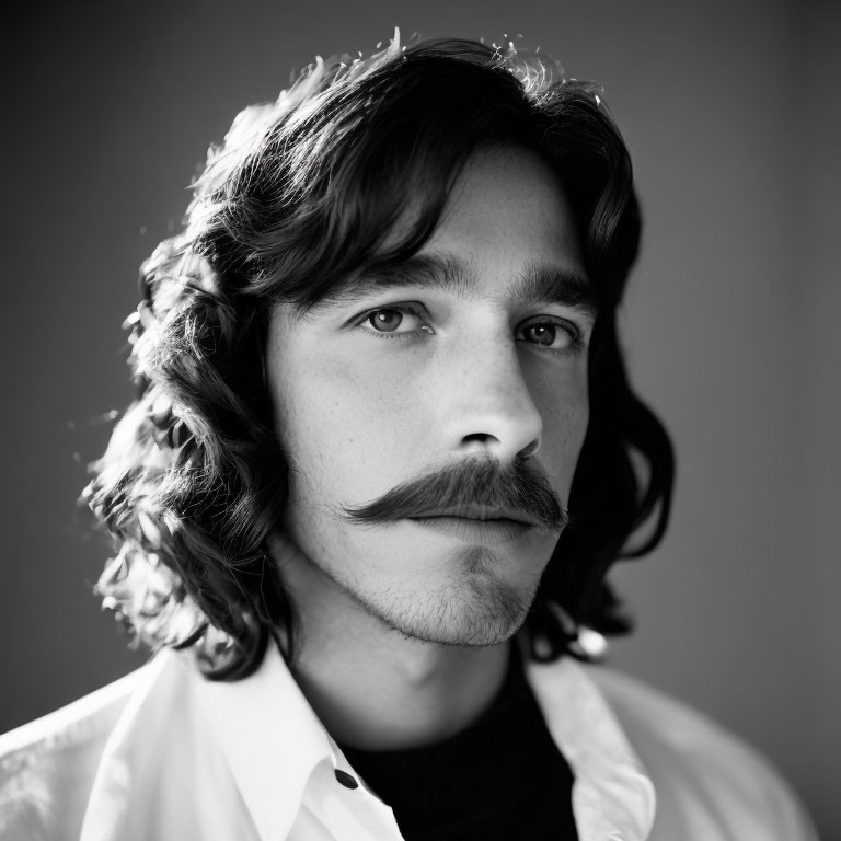 Monochrome portrait of man with curly hair and mustache in white shirt and dark sweater.