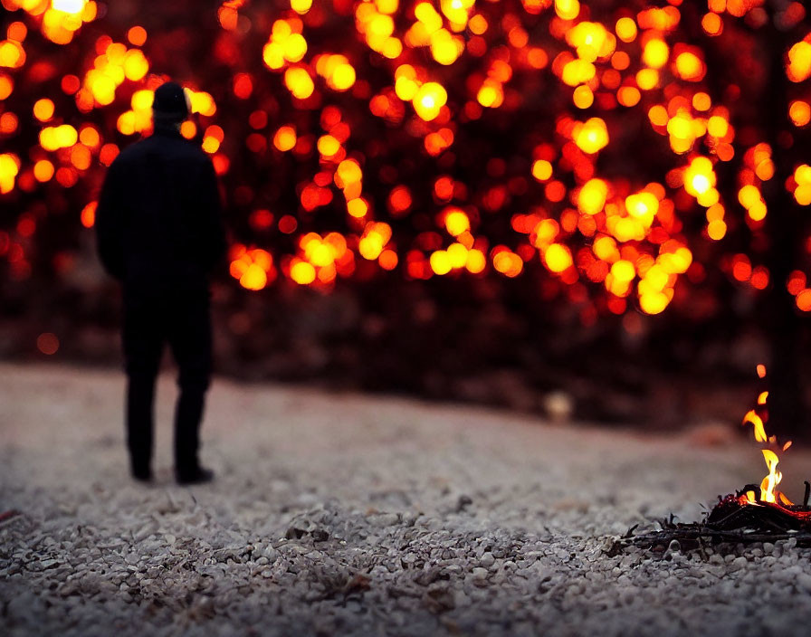 Individual standing in front of warm glowing lights with flickering flame in foreground