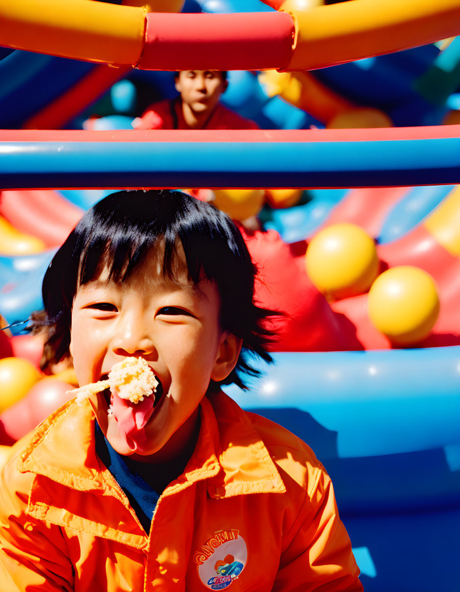 Child in Orange Jacket Enjoying Snack at Colorful Bouncy Castle