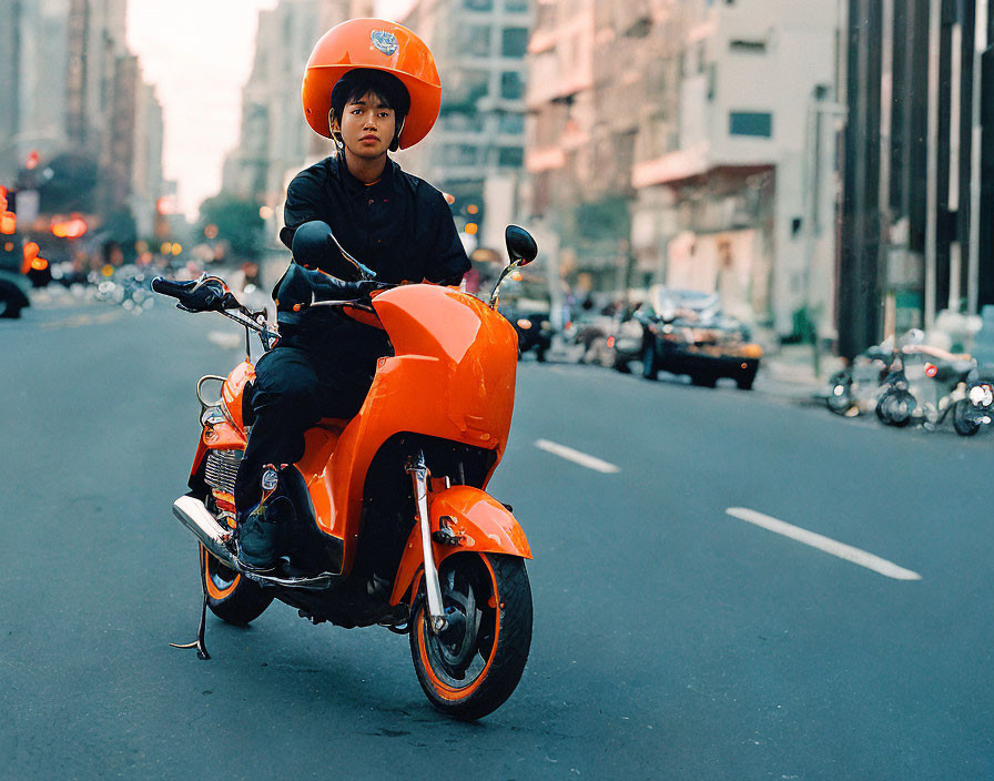 Person in black outfit on orange scooter in city street with cars