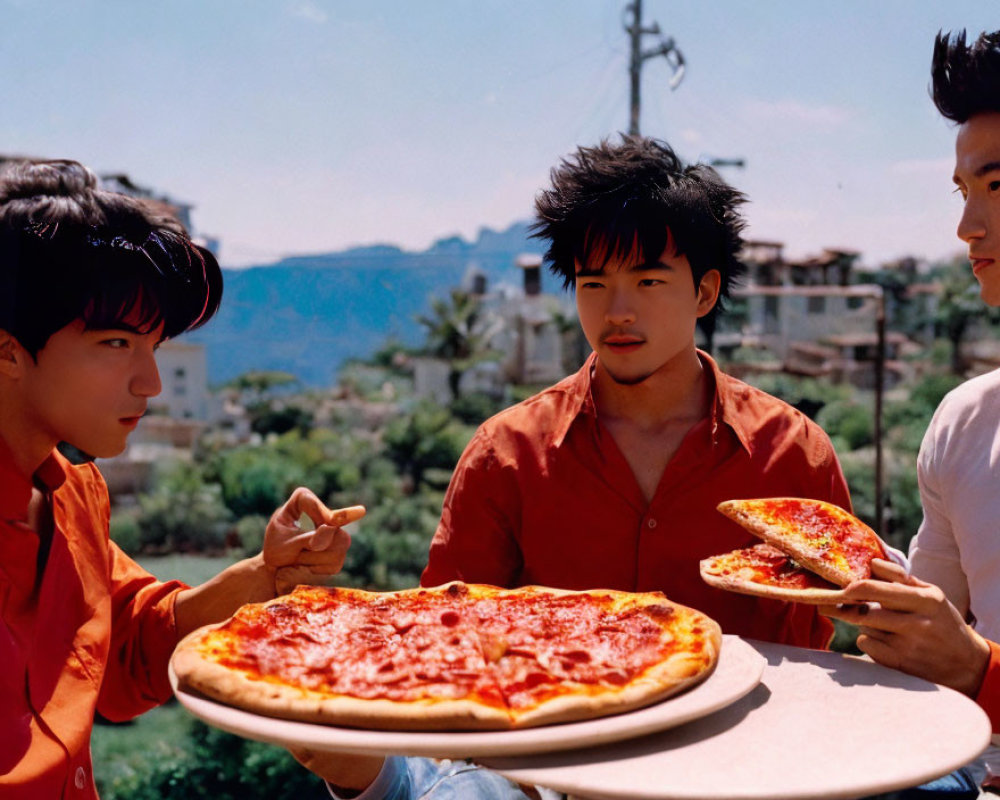 Three people eating pizza outdoors with greenery and mountains.