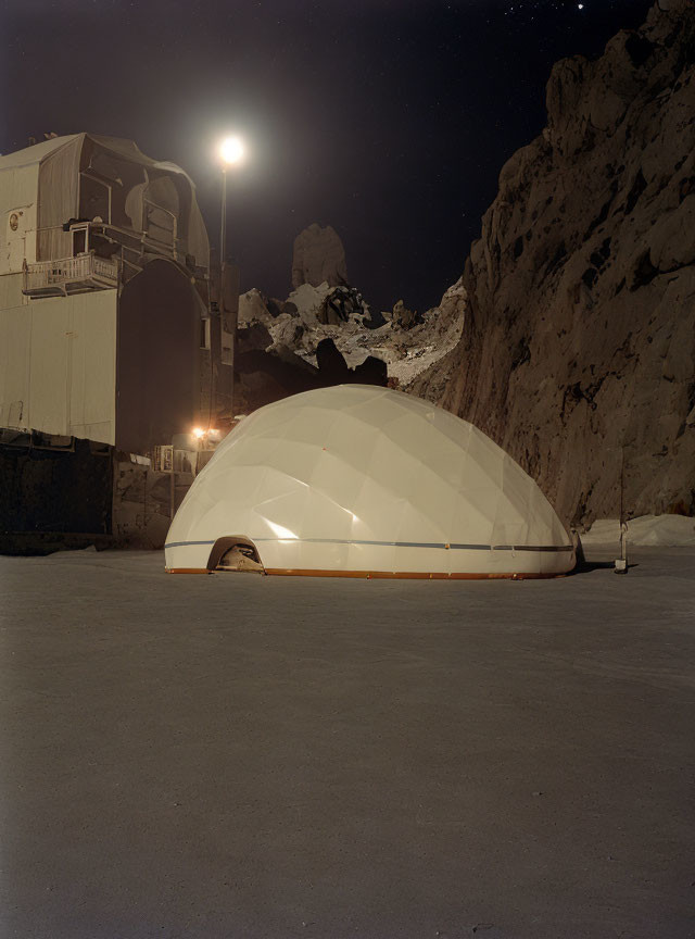 Geodesic dome illuminated in snowy landscape with mountain and buildings at night