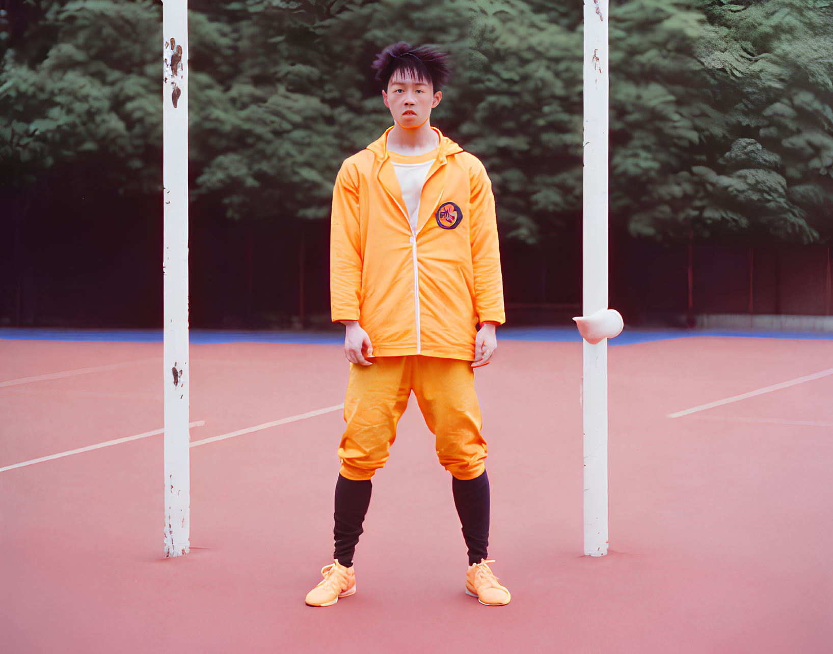 Vibrant orange tracksuit on person standing on red soccer court