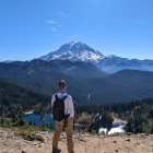 Hikers with backpacks in forested mountain landscape with snow-capped peak