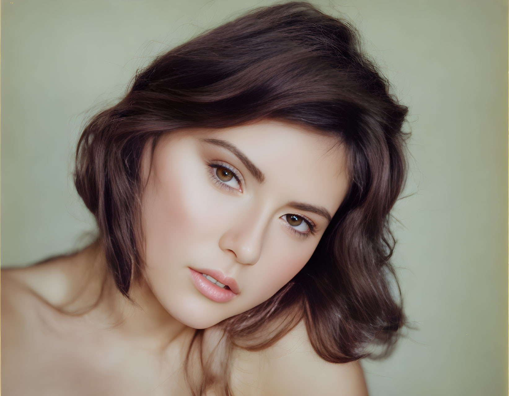 Young woman portrait with dark hair and fair skin on soft green backdrop