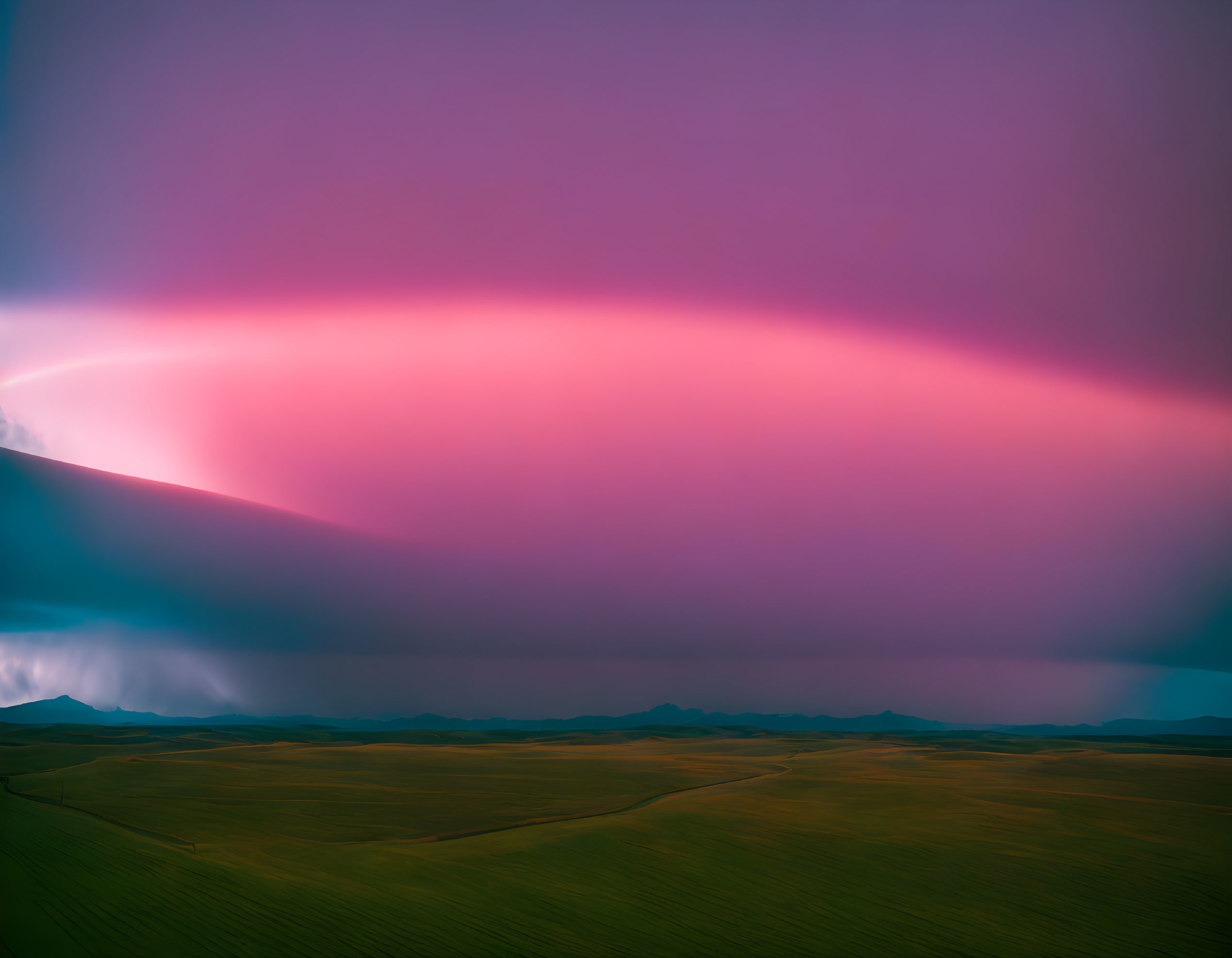 Expansive pink and purple sky over vast field with storm clouds.