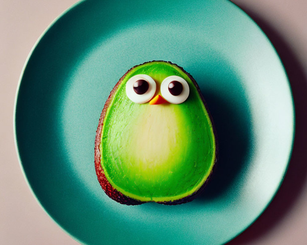 Cartoonish avocado with googly eyes on teal plate against pink background