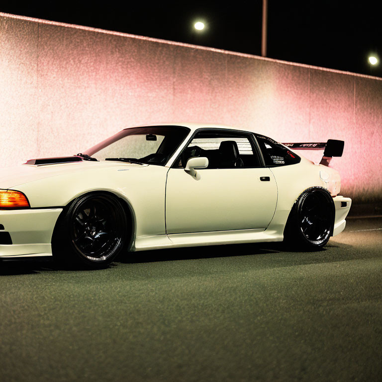 White Sports Car with Black Wheels Parked at Night under Streetlights and Glowing Pink Wall