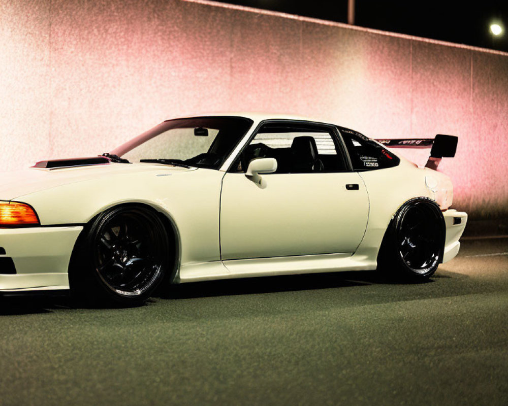 White Sports Car with Black Wheels Parked at Night under Streetlights and Glowing Pink Wall