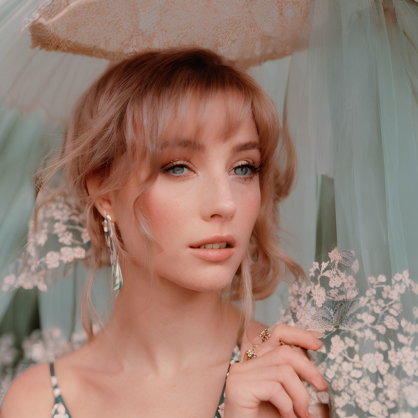 Blonde woman in lace hat and floral dress under blue veil