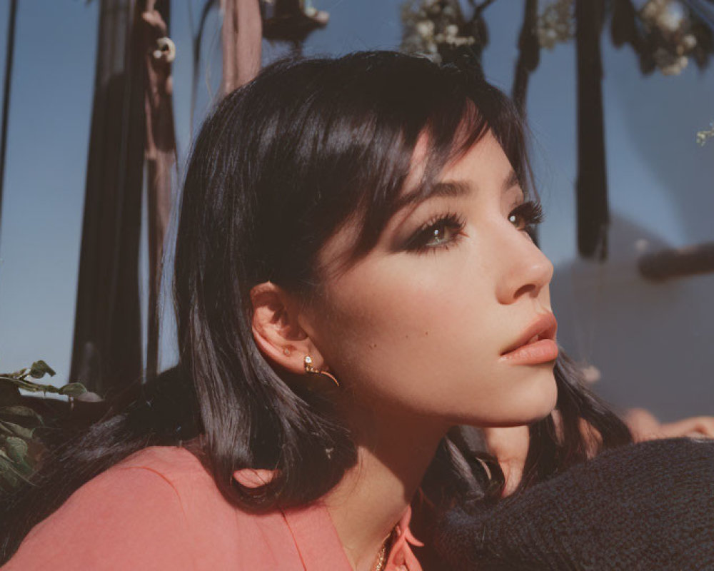 Dark-haired woman in coral top and earrings gazes at flowers and ropes