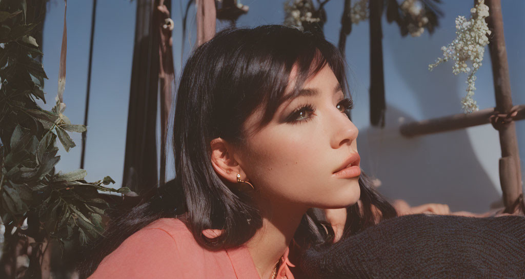 Dark-haired woman in coral top and earrings gazes at flowers and ropes