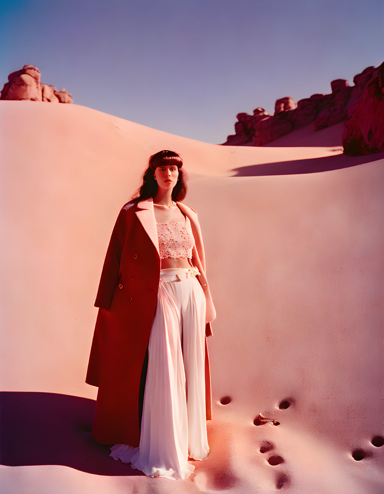 Woman standing on pink sand dune in white outfit with rocky background